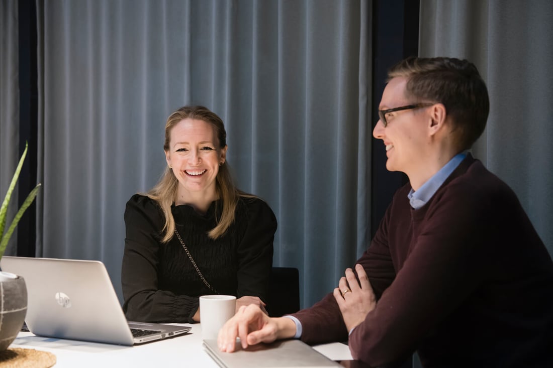 Kvinna och man sitter vid ett bord på en arbetsplats och ler