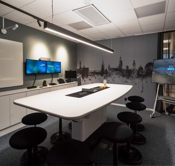 Ett modernt konferensrum utrustat med en whiteboard, ett konferensbord och flera skärmar på väggen.