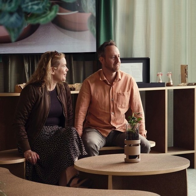 två människor runt ett bord i ett modernt framtidsinspirerat mötesrum. i mitten av bordet finns en ai-agent